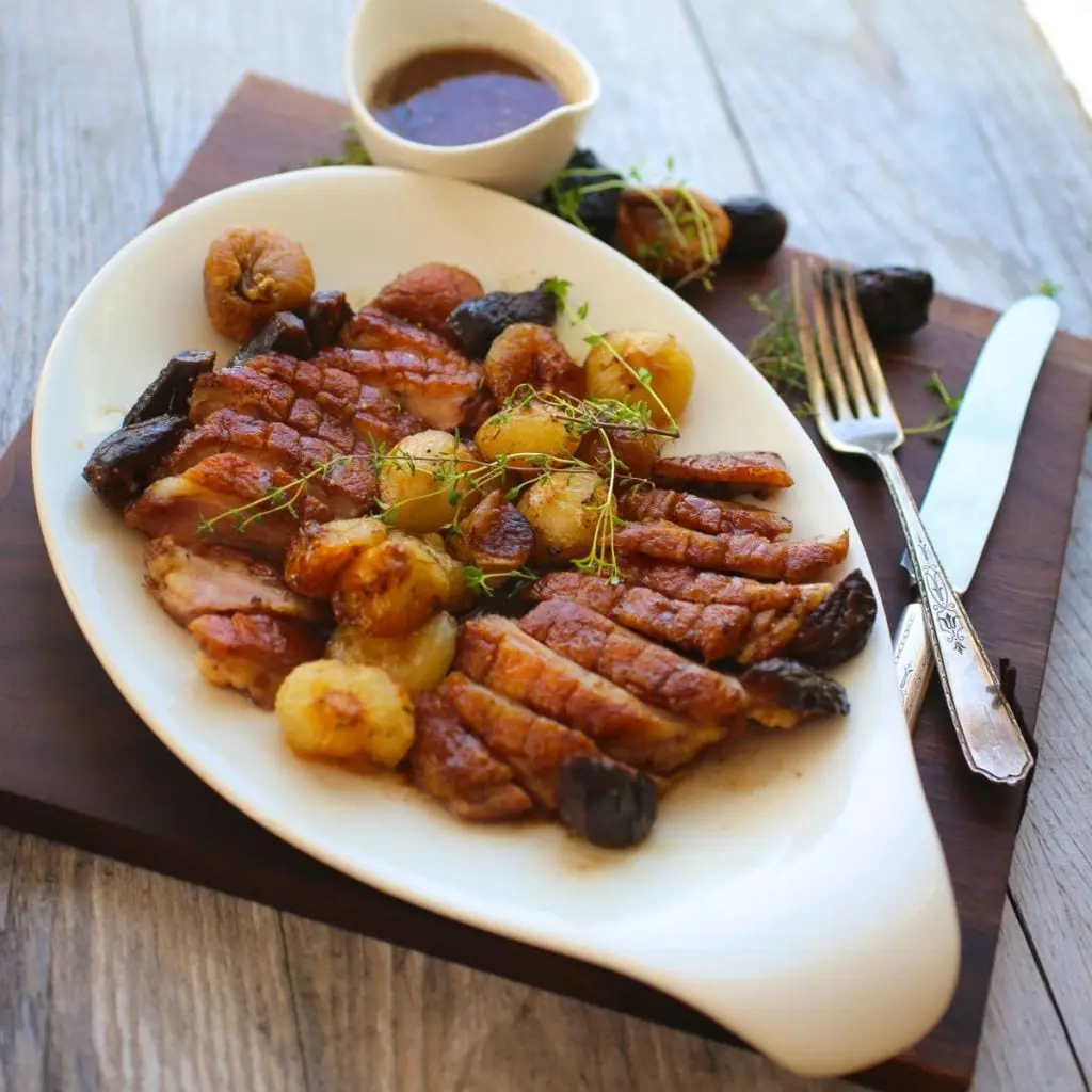 A platter of sliced cooked duck breasts with figs