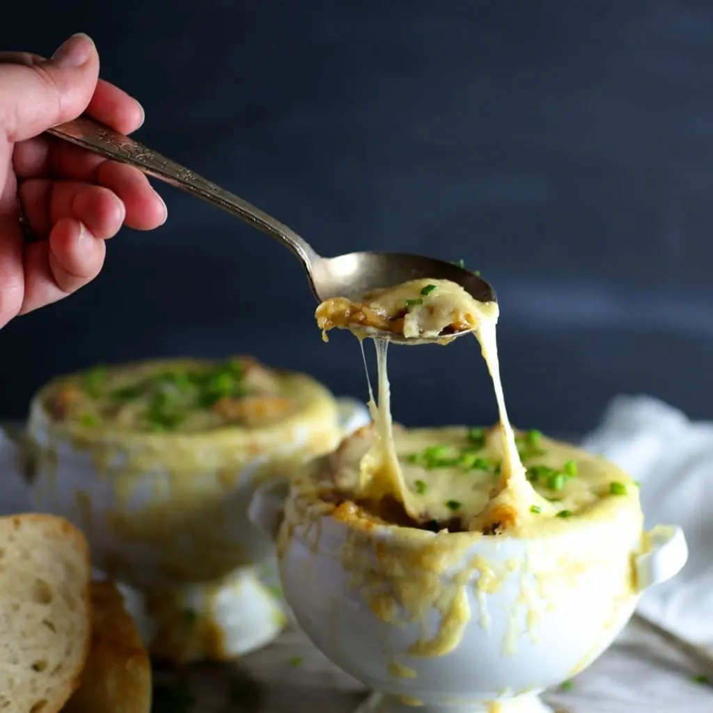 A spoon lifting a cheesy strand from French onion soup in a bowl