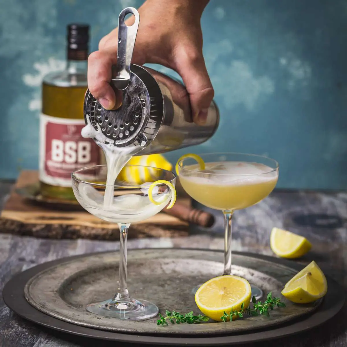 Pouring a cocktail through a strainer into a coupe glass