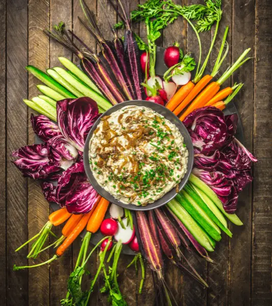 A bowl of onion dip surrounded by colorful veggies