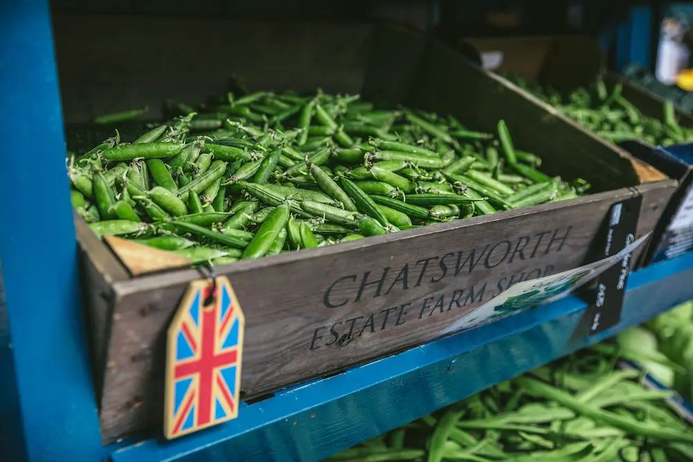 A farmer's market shelf with a wooden box of snap peas. The label reads "Chatsworth Estate Farm Shop"