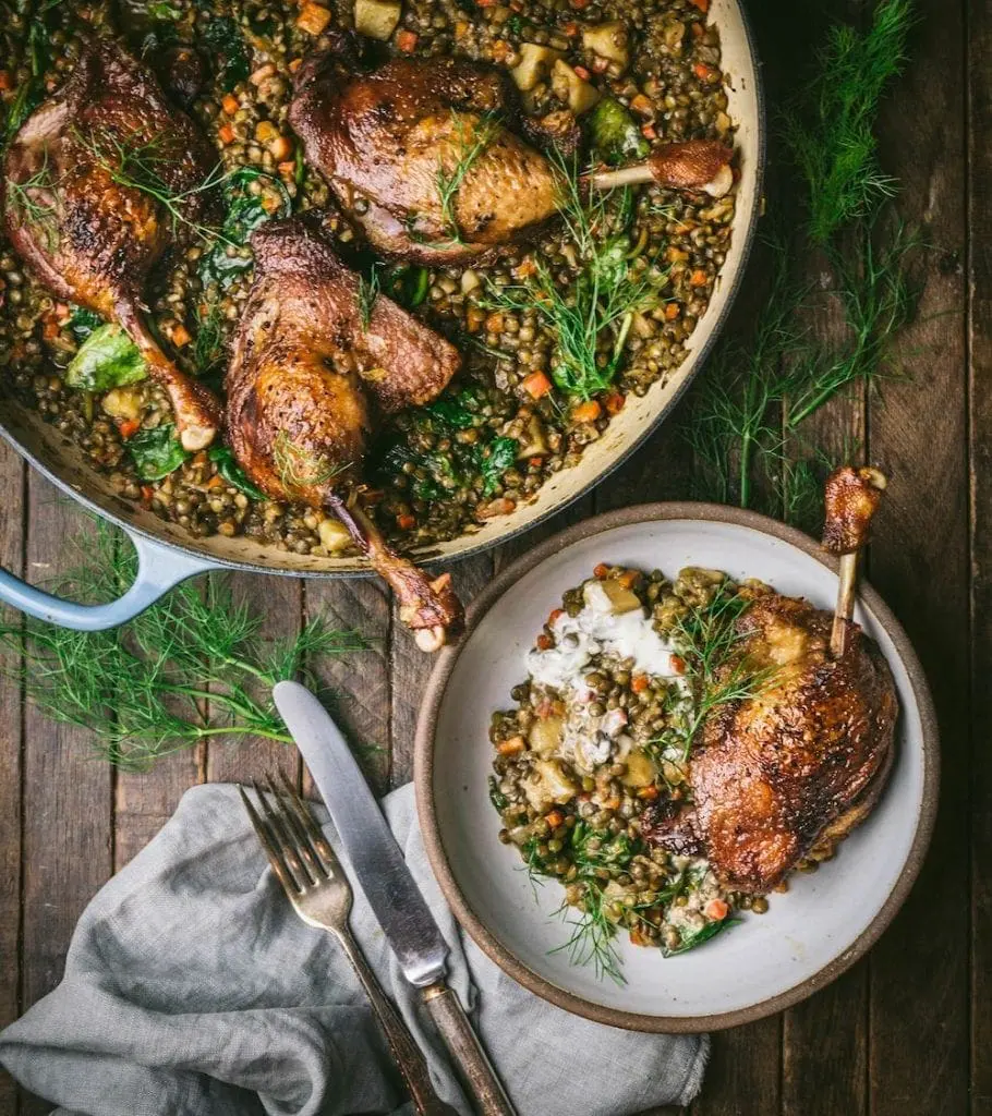 A braised and a small plate on a table, with cooked duck legs and lentils arranged in them