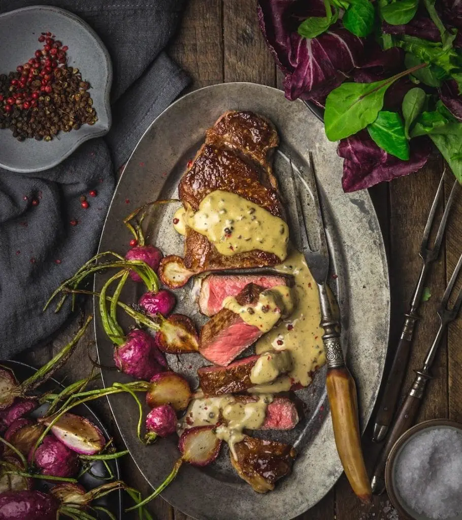 A pewter plate of sliced steak with sauce and radishes arranged on the side