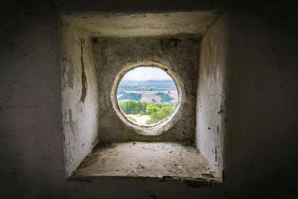 The view through a small round stone window onto a green English field