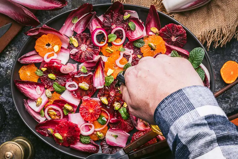 A hand pouring olive oil over a citrus salad