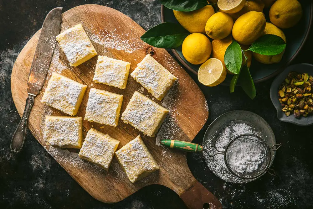 Magic lemon custard cake, cut into slices and powdered with sugar, next to a bowl of lemons
