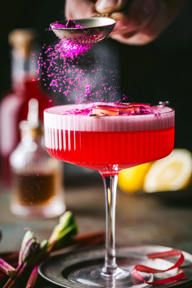 Sprinkling berry powder garnish on Rhubarb Cocktail