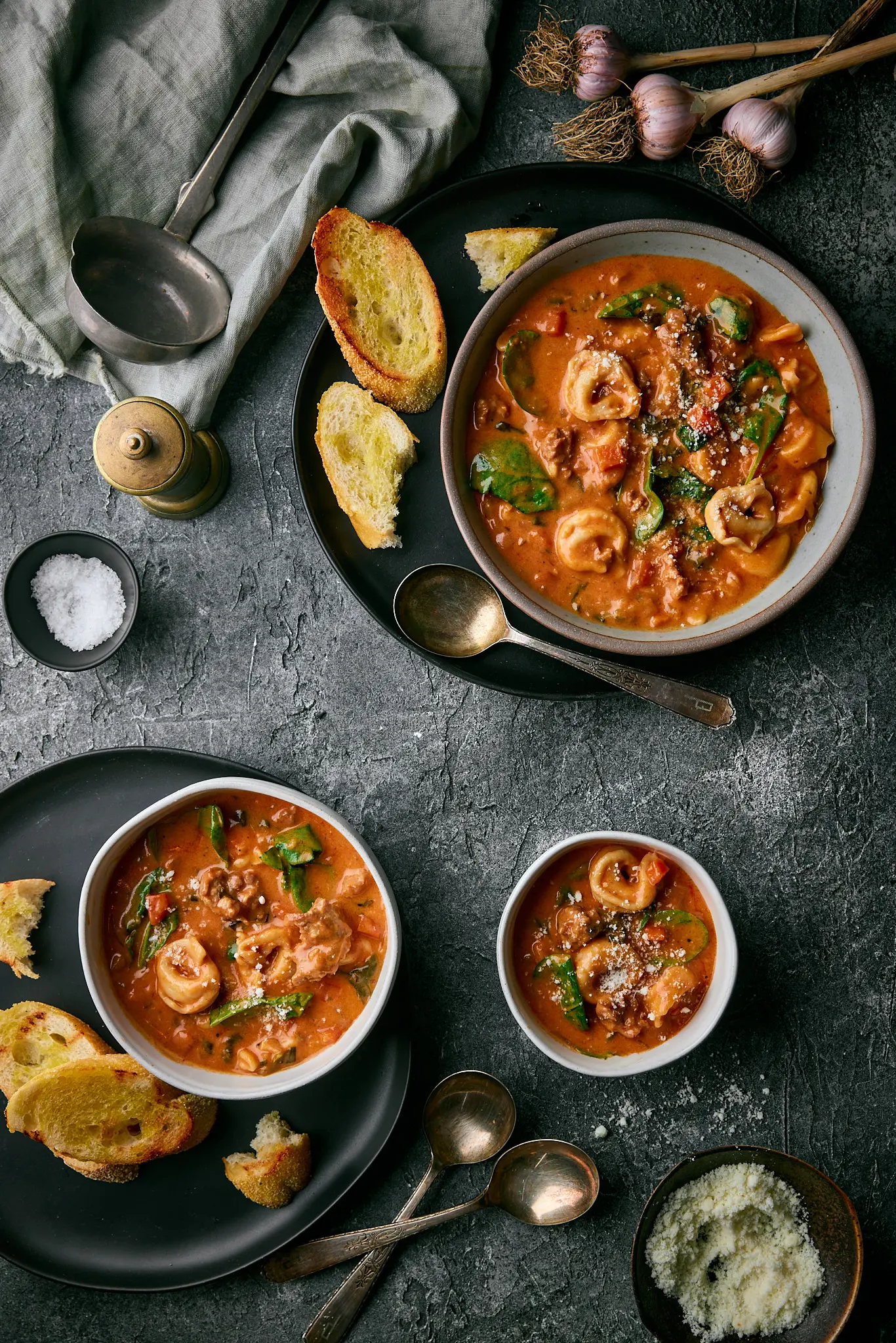 Tortellini soup in bowls with hunks of bread, spoons, salt and pepper.