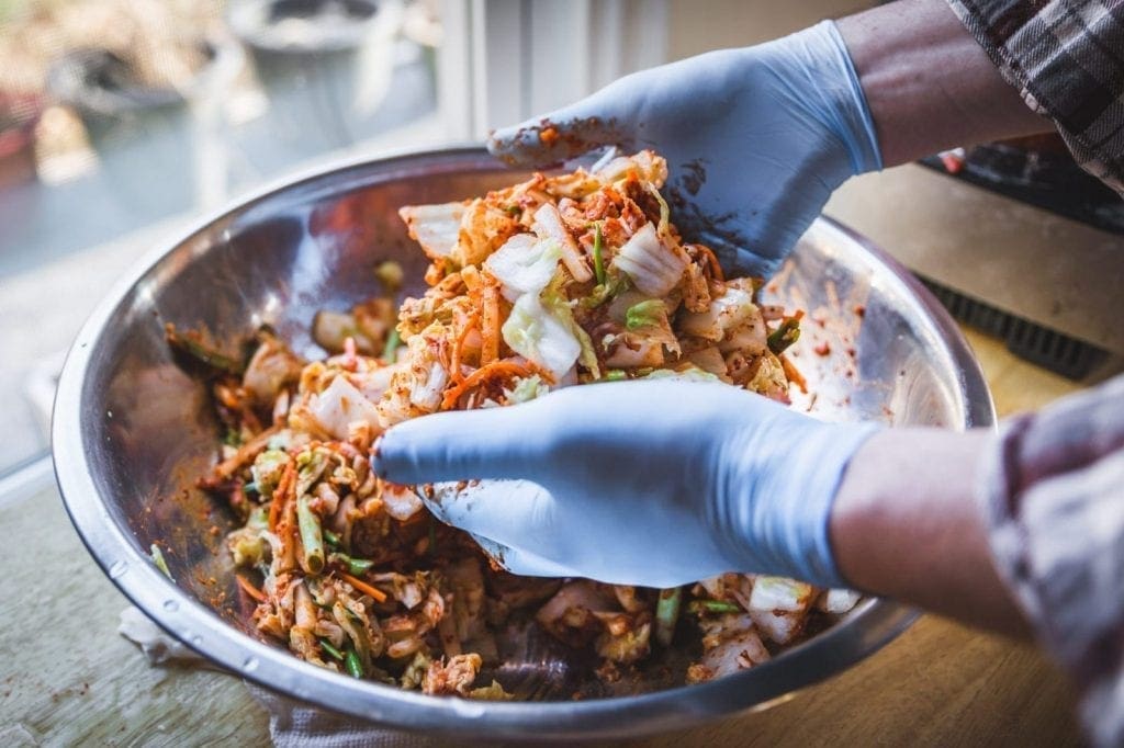 Gloved hands mixing kimchi in a big bowl