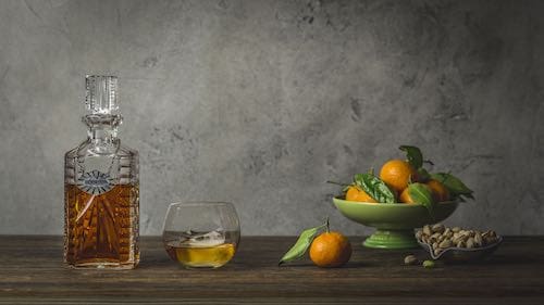 A decanter of bourbon next to a dish of oranges