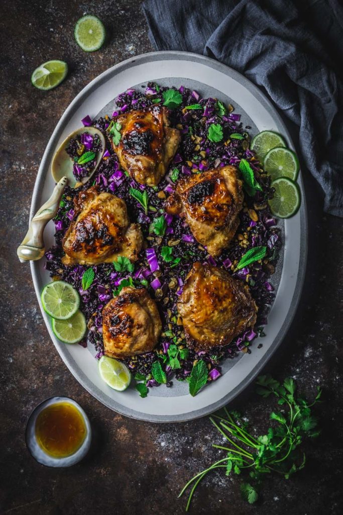 Chicken thighs nestled in black rice on a platter