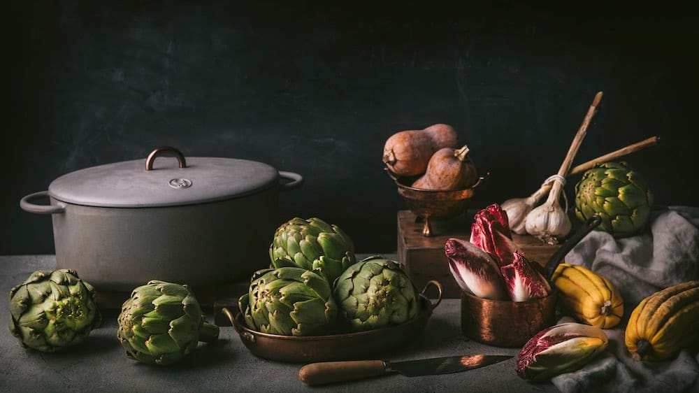 An arrangement of vegetables in pots and bowls next to a Dutch oven