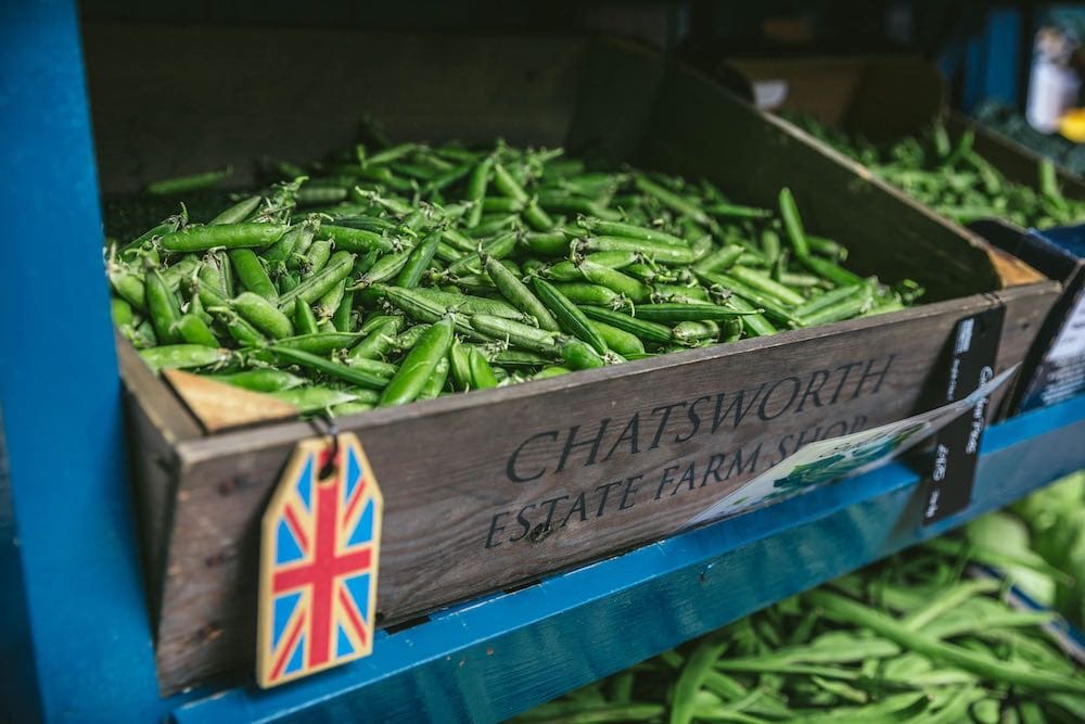 A farmer's market shelf with a wooden box of snap peas. The label reads "Chatsworth Estate Farm Shop"