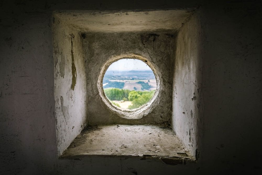The view through a small round stone window onto a green English field