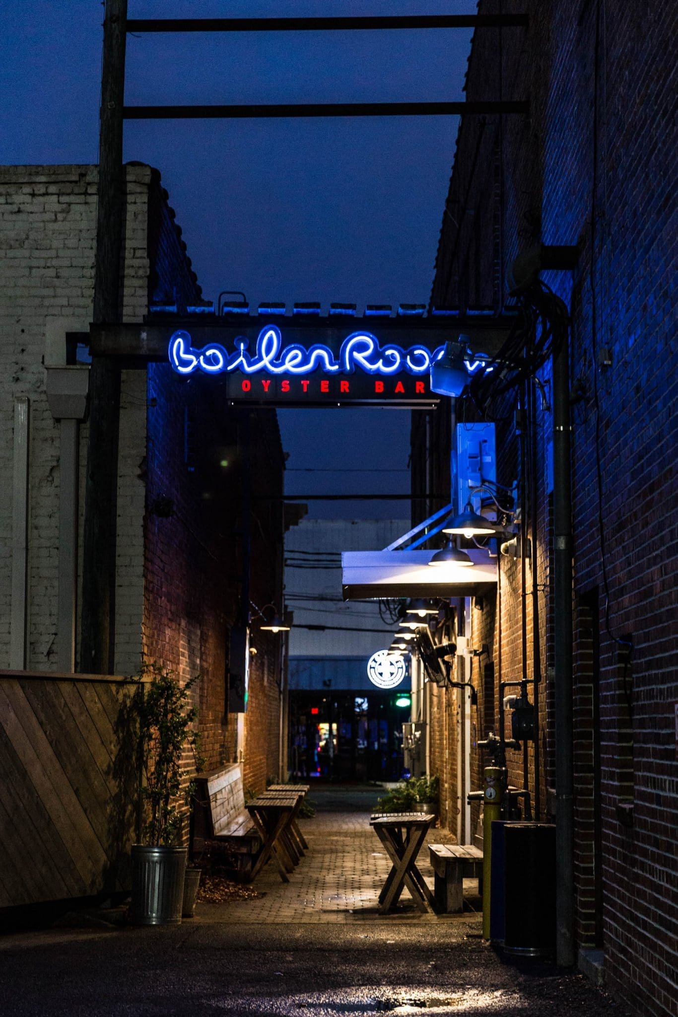 An evening shot of an alleyway with a restaurant sign and tables. The sign reads "Boiler Room Oyster Bar"