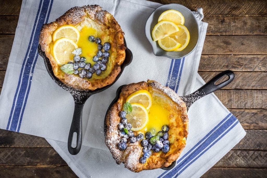 Two puffy Dutch Babies with curd and berries in little cast iron pans