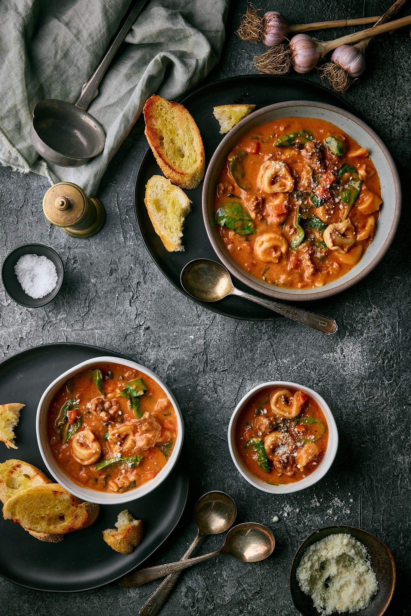 Tortellini soup in bowls with hunks of bread, spoons, salt and pepper.