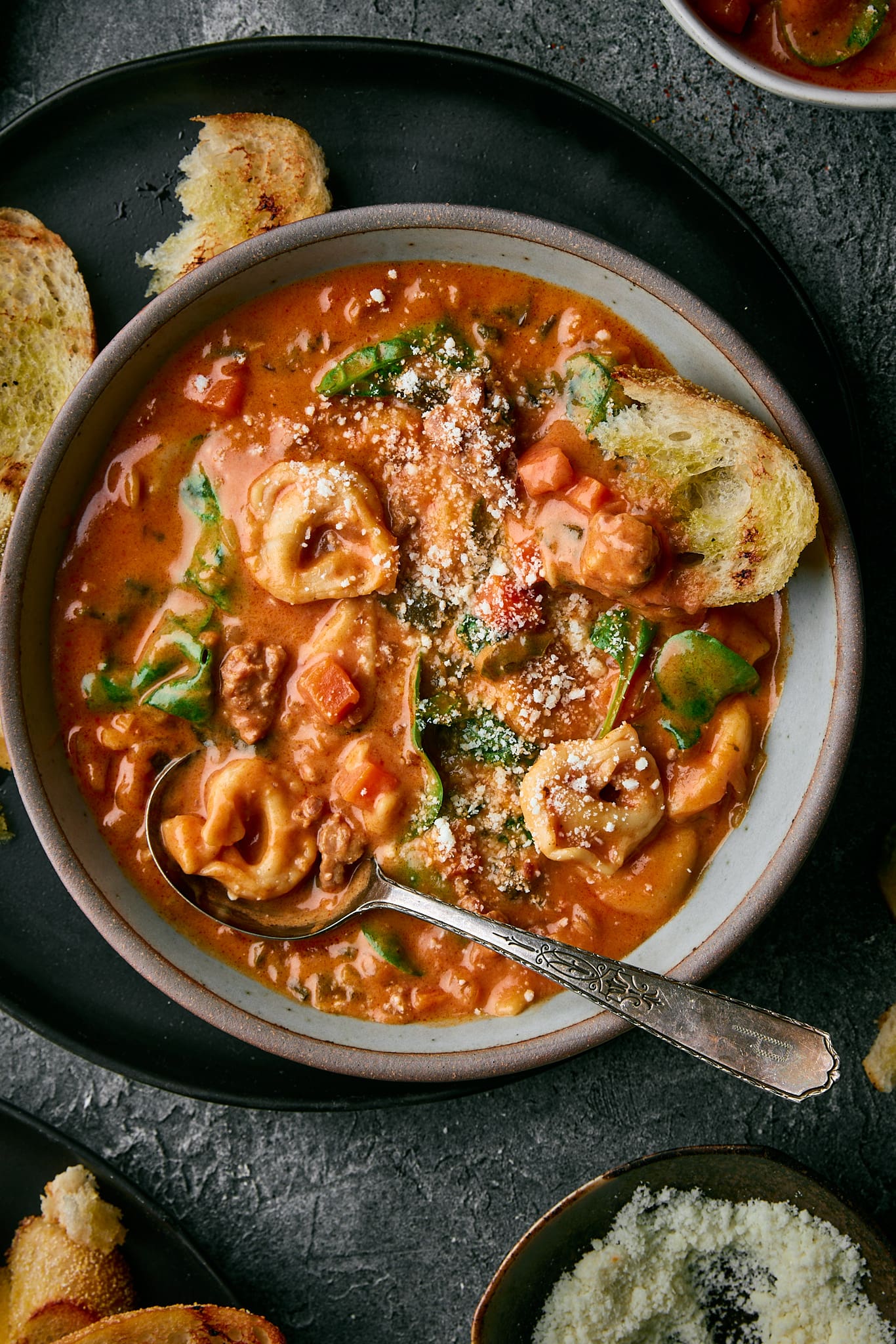 A bowl of tortellini soup with a hunk of bread in it